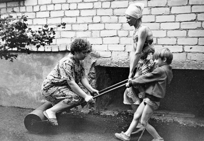 Женщины и ребенок катают асфальт катком возле дома.