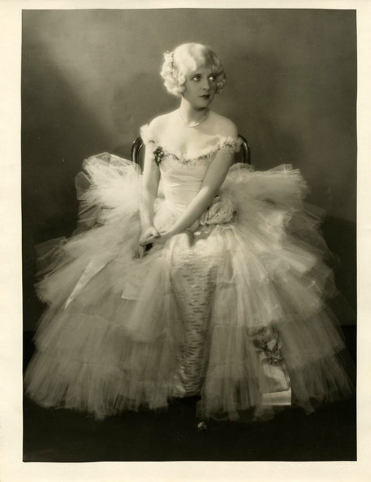 Актриса в платье из тюлевой ткани и атласа, украшенное вышивкой.