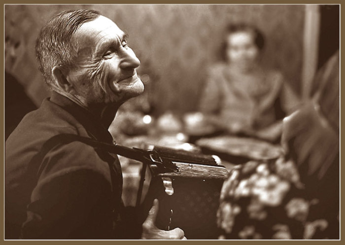 Пожилой мужчина, играющий на тальянке в домашнем кругу. 