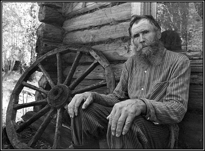 Пожилой мужчина, сидящий возле своего дома. 