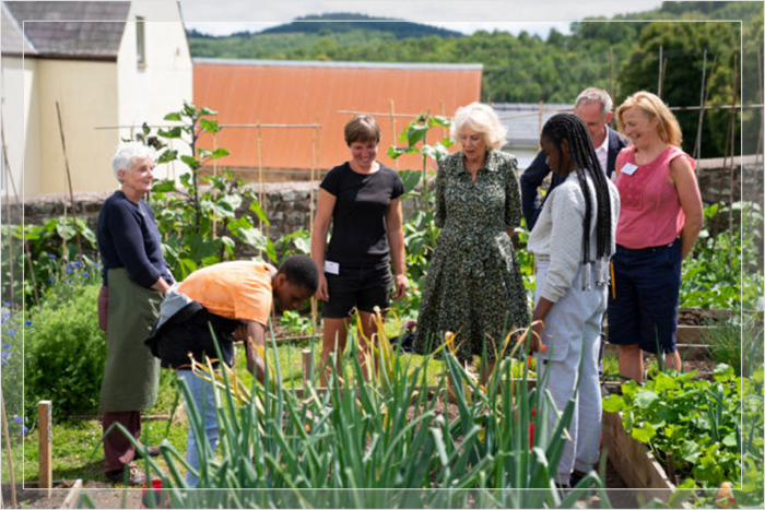 Камилла, королева-консорт, разговаривает со студентами в огороде во время посещения жилой фермы в долине Уай, Уэльс, 6 июля 2022 года.