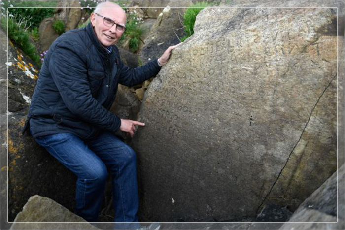 Французский местный советник, отвечающий за историческое наследие, Мишель Погам, позирует 7 мая 2019 года, показывая надписи, состоящие из неразборчивых слов, на скале в бретонской деревне Плугастель-Даулас.